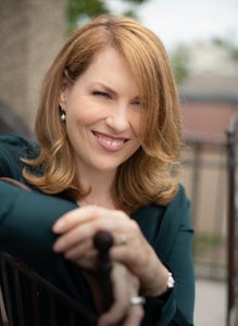 23-JoBrowning-headshot-518x708 A woman with auburn hair smiling and wearing an olive green top