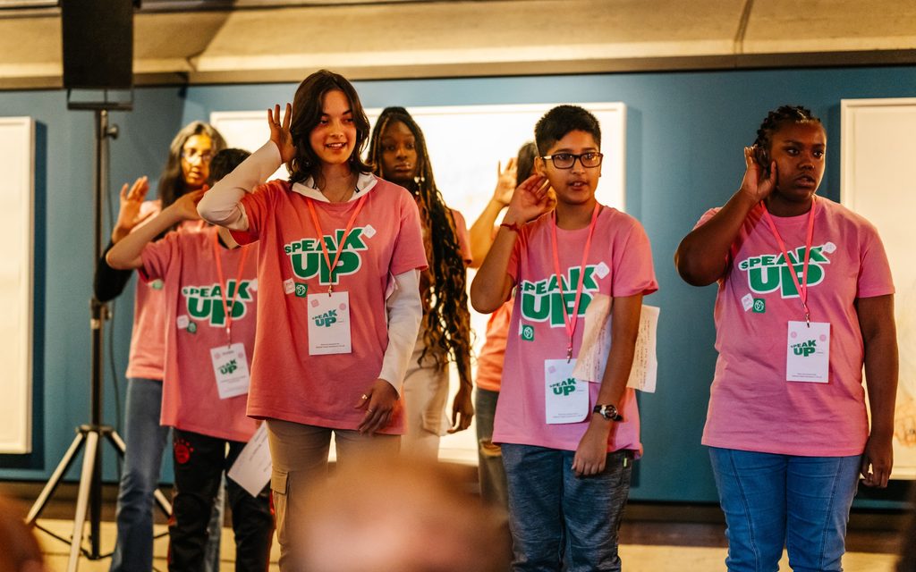 23-SpeakUp-GetTogether-Council1Namesremoved-2000x1250-MatthewKaltenborn A group of young people wearing pink t-shirts with the words 'Speak Up' written on them - they are speaking British sign language