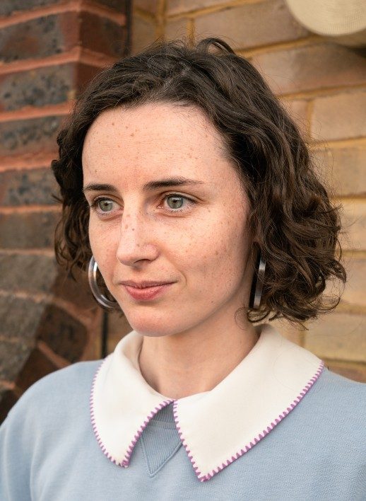 Bethan-Wall-Headshot-KarolyTendl-518x708 A photograph of a person with a wavy bob haircut and a wearing a white collar shit with a pale blue jumper