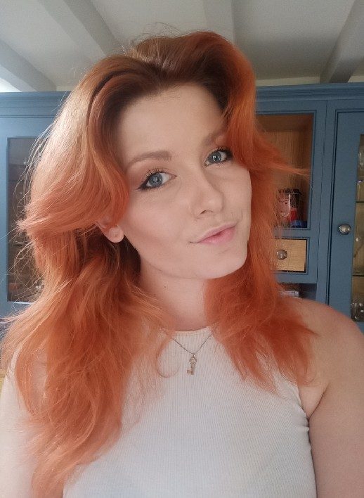 Biz-Sutton-Headshot-BizSutton-518x708 A person with long pale orange hair wearing a white sleeveless top