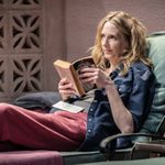 A woman sitting in a green lounge chair reading a book called Daniel Deronda by George Eliot.