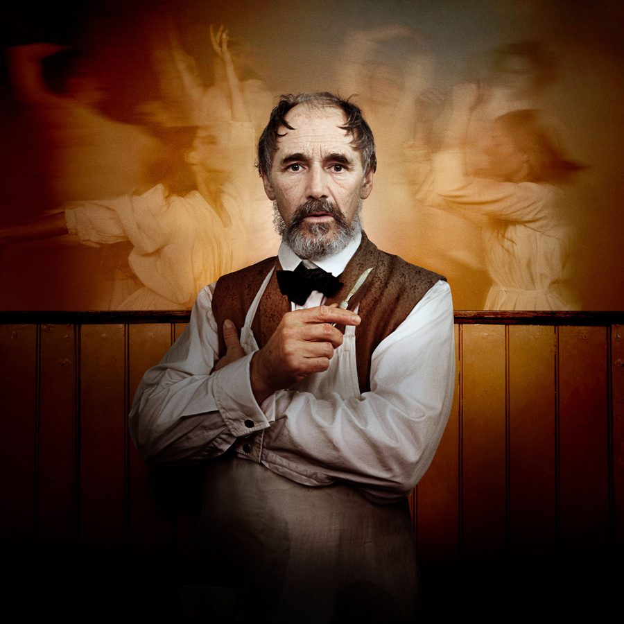 Dr-Semmelweis-Harold-Pinter-Theatre-National-Theatre-2000x1000 Mark Rylance stares straight at us, arms folded, holding a scalpel. Behind him, a blurred image of women dressed in white, dancing.