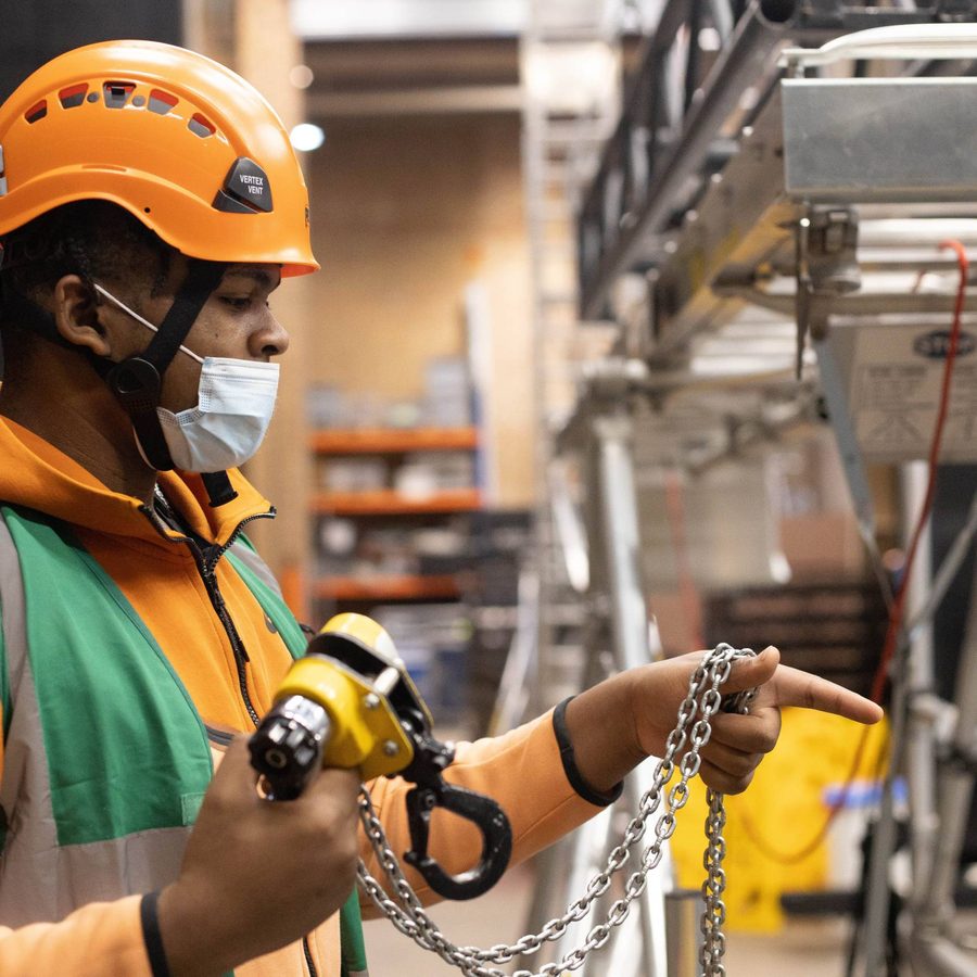 2022Young Techs-orangehatchain A Young Technician in an orange hard hat holding a piece of rigging