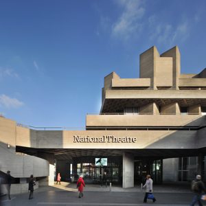 National-theatre-exterior-by-phillip-vile-2000x2000-Masthead-004 National Theatre building, main entrance exterior with name in raised lettering on the lower terrace balcony and people walking in the square in front.