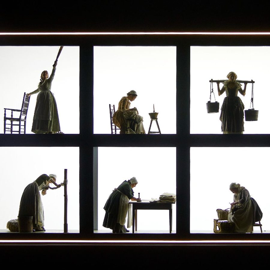 The-Welkin-set-National-Theatre-Photo-Brinkhoff-Moegenburg-masthead A grid structure with twelve rectangular compartments, each depicting a silhouette of a person engaged in different activities such as writing, carrying buckets, reading, and working with textiles against a brightly lit white background.