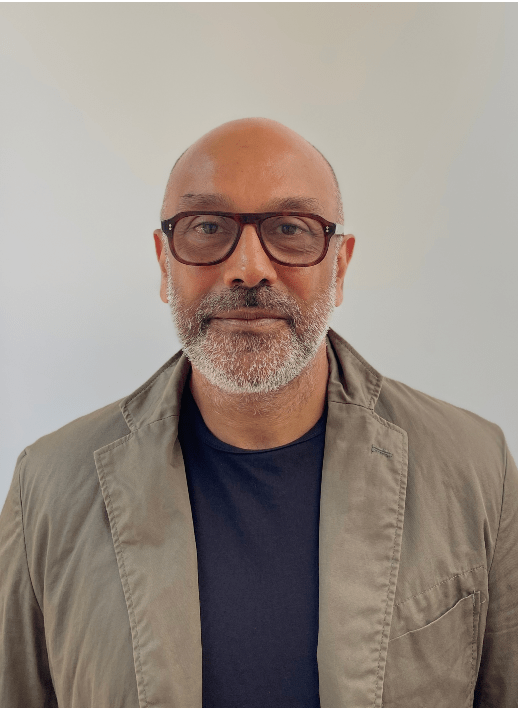 Nitin-Parmar-headshot-NitinParmar-518x708 A photograph of a person wearing glasses, with a grey-ish beard and wearing a beige jacket and navy blue t-shirt